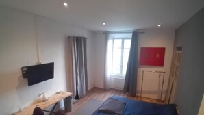 A bedroom with a bed, a desk, a chair, a TV, and a window with curtains.