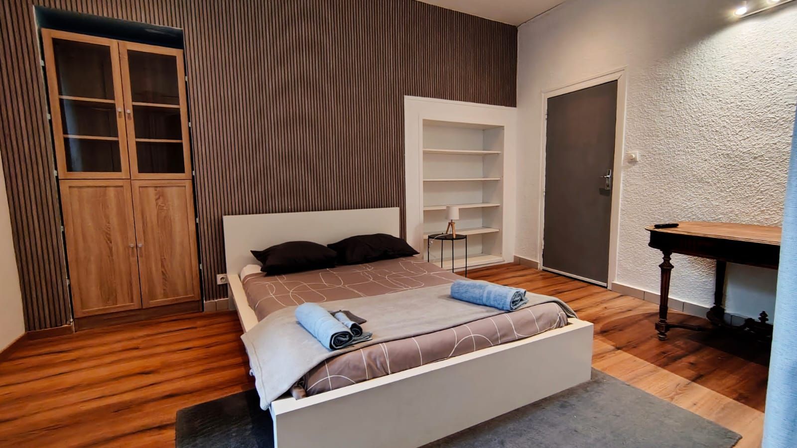 A bedroom with a bed, a wardrobe, a desk, and a shelving unit.