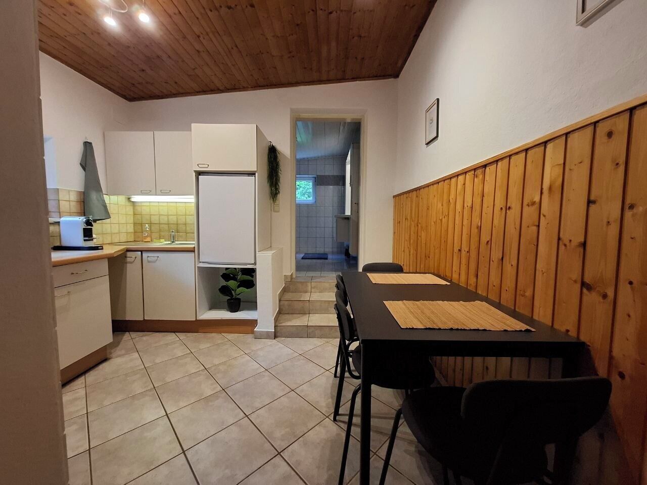 Una cocina compacta con gabinetes blancos, un comedor con mesa negra y techo de madera.