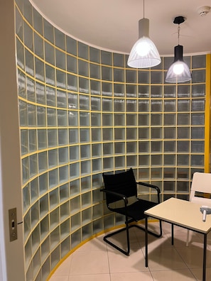 Une pièce dotée d’une cloison en verre incurvé, d’une chaise noire, d’une table blanche et de deux lampes suspendues.