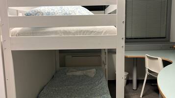 A bunk bed with a desk and chair, a window with blinds, and a radiator.