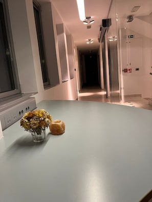 Un pasillo con una puerta de cristal, un pequeño jarrón con flores y un donut sobre una mesa.
