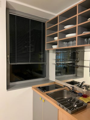 A kitchen with a built-in stove, a sink, and a window with blinds.