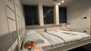 Ett modernt sovrum med en säng, ett sängbord och ett litet bord med en vas och ett ljus.