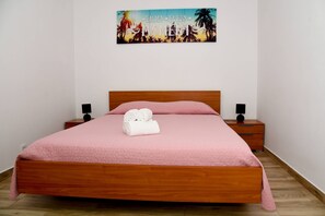 A neatly made bed with a pink quilt, two bedside tables with lamps, and a wall art depicting a tropical scene. - Sunny Pearl Apartment (Caniço)