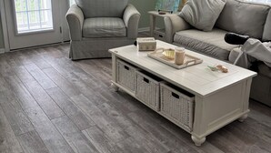 Un salon avec un canapé gris, un fauteuil, une table basse avec des plateaux et des paniers en osier.