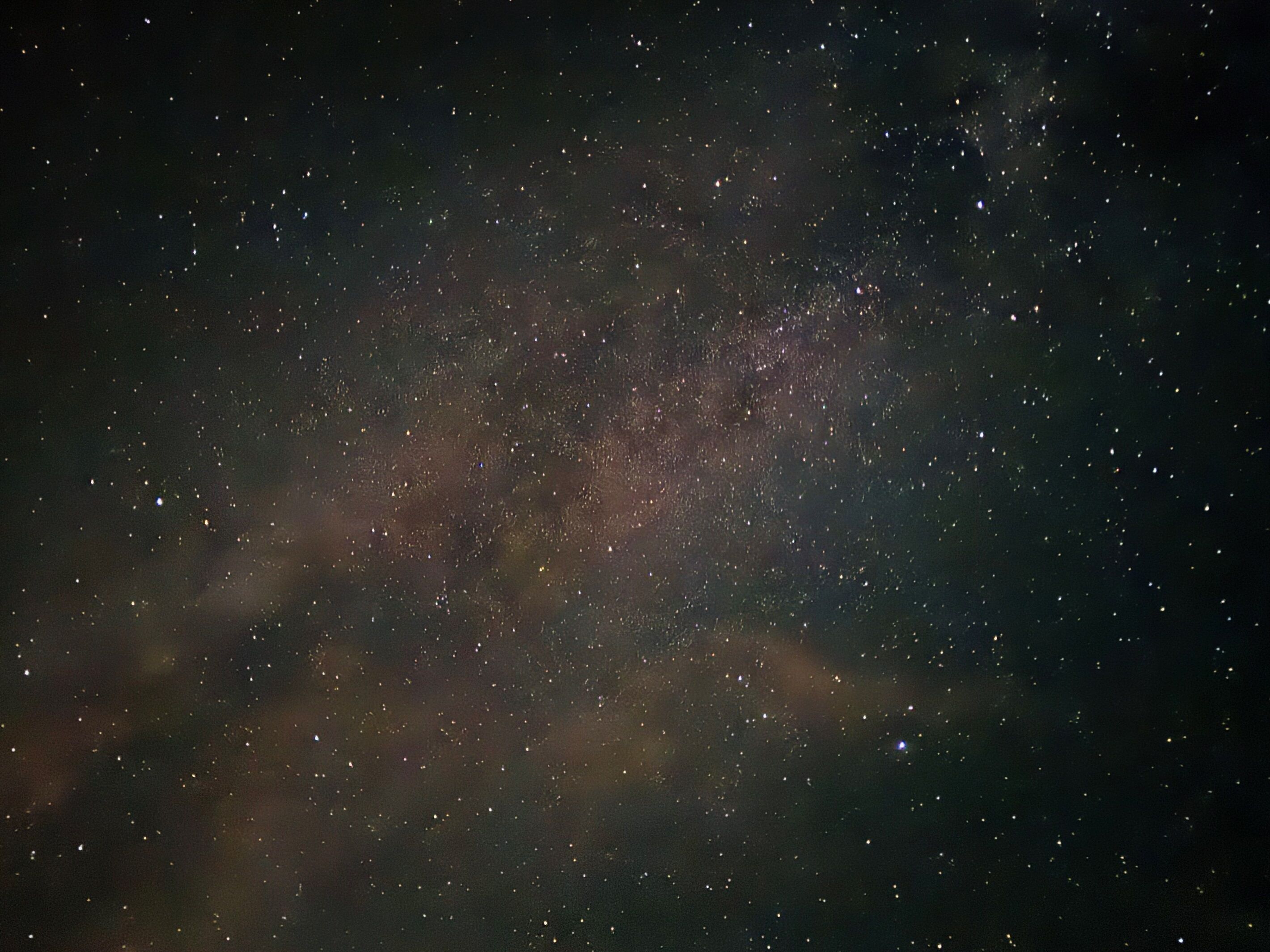 A starry night sky with a dense cluster of stars and a faintly visible galaxy.
