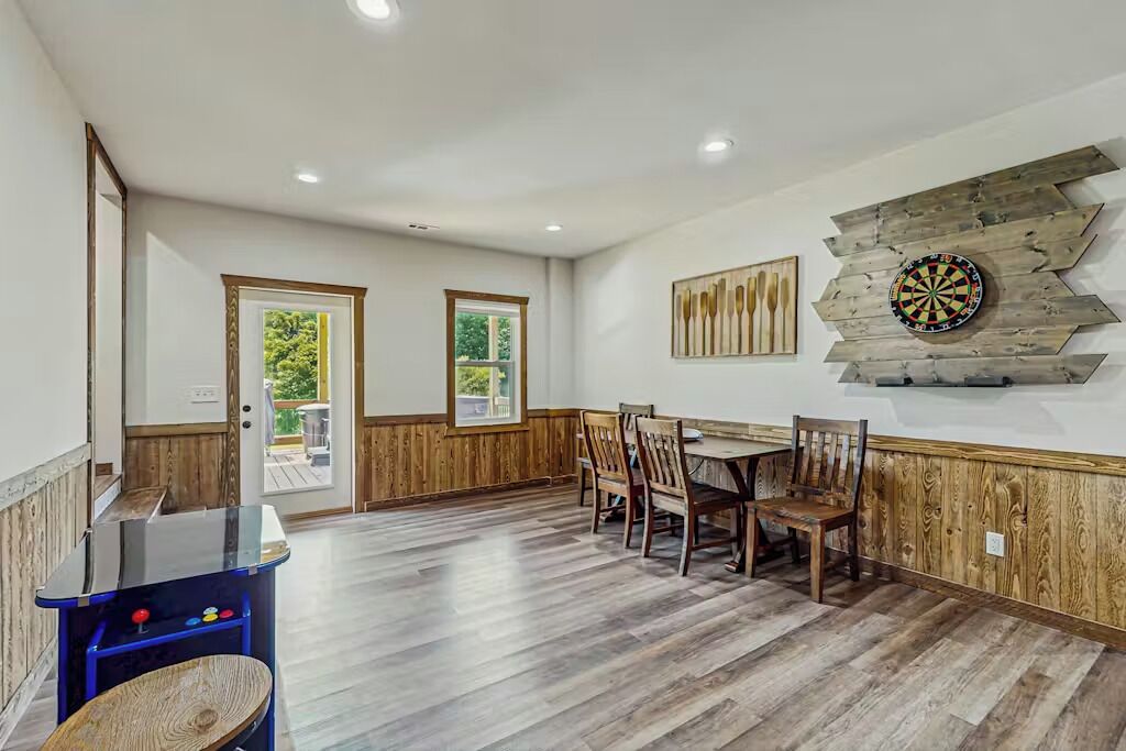 A dining area with wooden flooring, a table, chairs, and a dartboard on the wall.