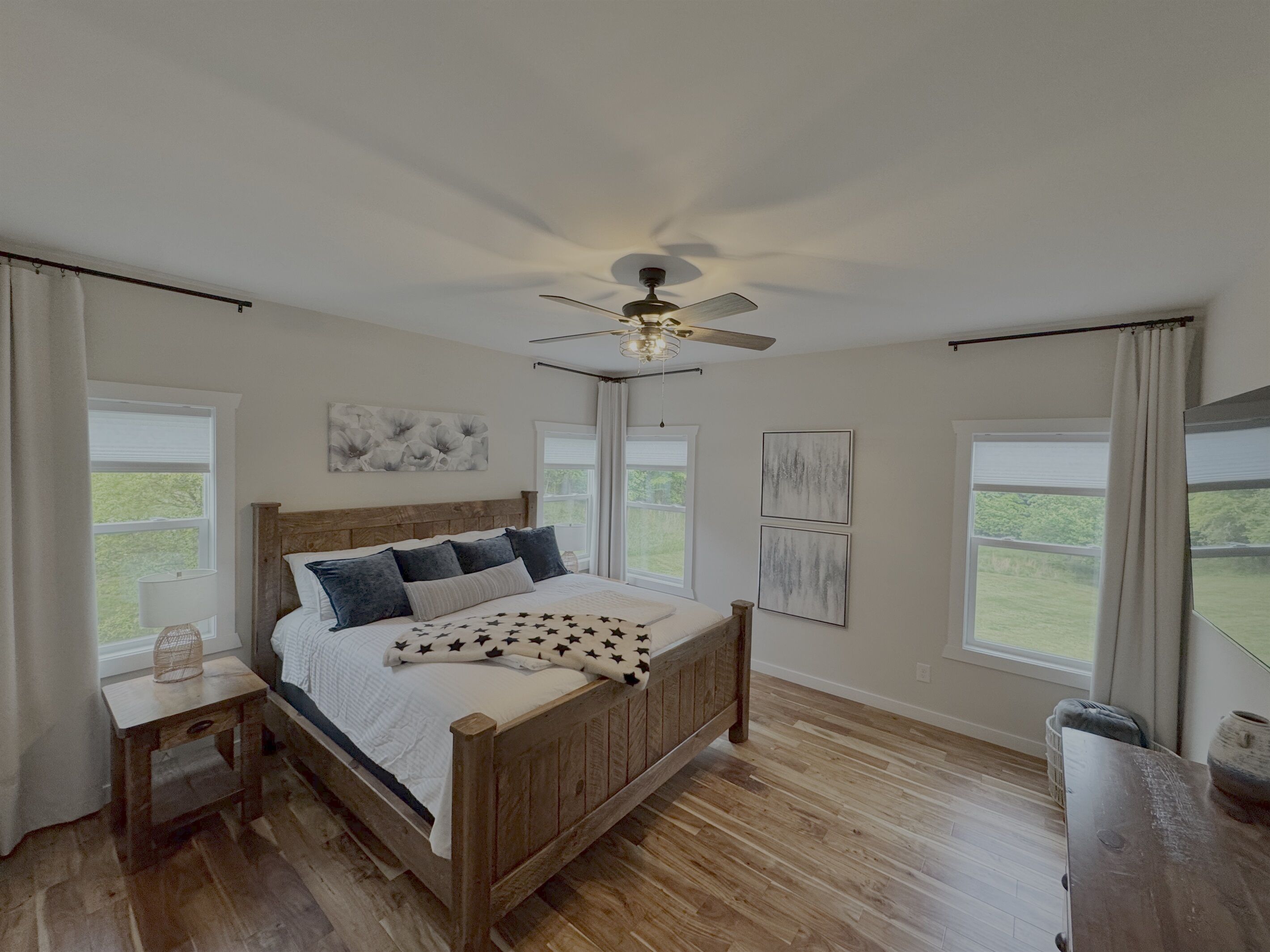 A bedroom with a wooden bed, a ceiling fan, and large windows.