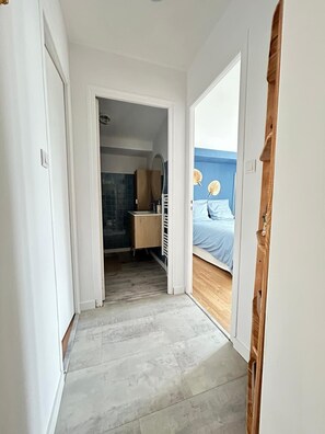 Een gang die leidt naar een slaapkamer met een bed, een dressoir en een spiegel.