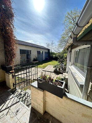 Une cour avec un portail en mĂ©tal, un bac Ă fleurs en bĂ©ton plantĂ©, un bĂątiment avec une fenĂȘtre et un ciel dĂ©gagĂ©.