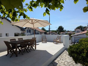 A patio with a table and chairs, a large umbrella, and a view of surrounding houses. - Family home in Anglet - Between forest, sea and golf course (Anglet)
