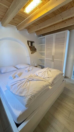 A bed with white linens, a wooden ceiling, and a built-in wardrobe with horizontal slats.