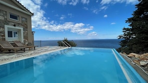 Une piscine avec vue sur la mer, des chaises longues et un bĂątiment en pierre.