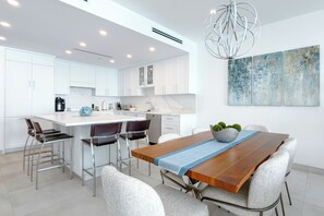 A modern kitchen with white cabinets, a wooden dining table, and bar stools. - Beachcomber 28 by Grand Cayman Villas (Seven Mile Beach)