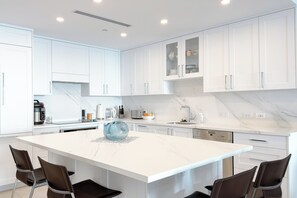 A modern kitchen with white cabinetry, a marble countertop, and a central island with chairs. - Beachcomber 28 by Grand Cayman Villas (Seven Mile Beach)