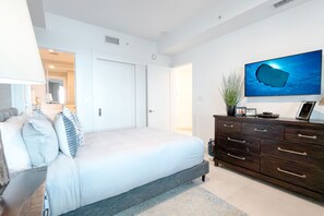 A bedroom with a bed, a dresser, a television, and a wall-mounted artwork. - Beachcomber 28 by Grand Cayman Villas (Seven Mile Beach)