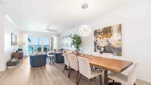 A spacious living area with a wooden dining table, white chairs, and a large abstract painting on the wall. - Beachcomber 7 by Grand Cayman Villas (Seven Mile Beach)