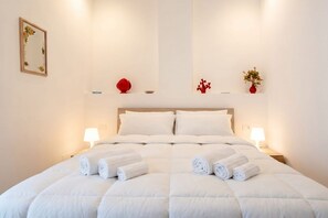 A neatly made bed with rolled towels, a headboard, bedside lamps, and decorative items on the wall. - Lucia Italian Living (Bari)