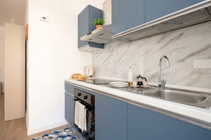 A modern kitchen with a marble backsplash, a stainless steel sink, and a built-in oven. - Lucia Italian Living (Bari)