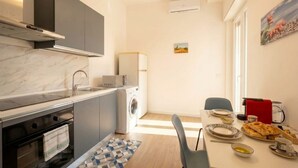 A compact kitchen with a built-in oven, a washing machine, and a dining area with a table set for two. - Lucia Italian Living (Bari)