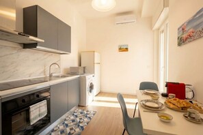 A compact kitchen with a built-in oven, a washing machine, and a dining area with a table set for two. - Lucia Italian Living (Bari)