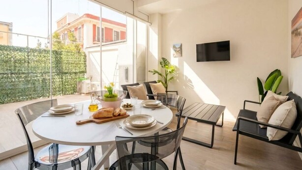A modern dining area with a round table, clear chairs, and a TV mounted on the wall. - Lucia Italian Living (Bari)