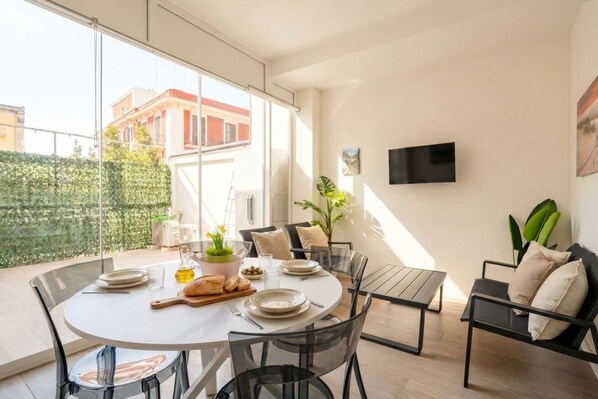 A modern dining area with a round table, clear chairs, and a TV mounted on the wall. - Lucia Italian Living (Bari)