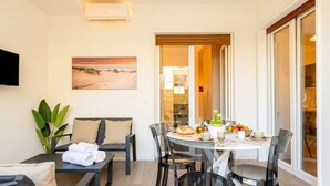 A modern room with a dining table set for two, a sofa, and a TV mounted on the wall. - Lucia Italian Living (Bari)