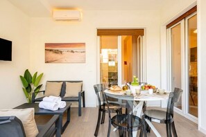A modern room with a dining table set for two, a sofa, and a TV mounted on the wall. - Lucia Italian Living (Bari)