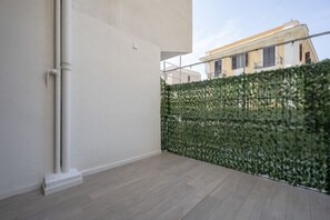 A room with a white wall, a wooden floor, and a green leafy privacy screen. - Lucia Italian Living (Bari)