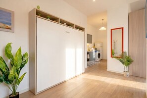 A modern interior with a wardrobe, potted plants, a kitchen area, and a mirror. - Lucia Italian Living (Bari)
