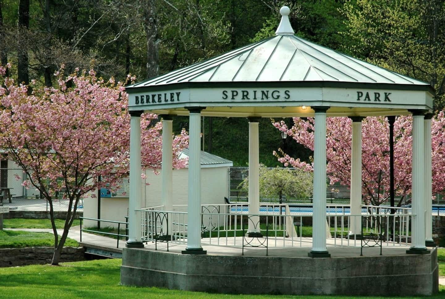 A gazebo with the words 'BERKELEY SPRINGS PARK' on its roof, surrounded by blooming trees.