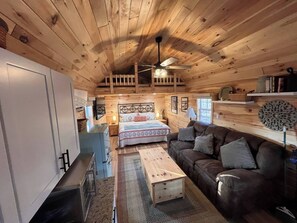 Un intĂ©rieur de chalet chaleureux avec une chambre en mezzanine, un espace de vie dotĂ© dâun canapĂ© et un coin repas.