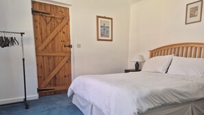 Une chambre avec une porte en bois, un lit avec une literie blanche, une table de chevet avec une lampe et un tableau encadré au mur.