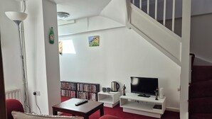 Un salon avec un tapis rouge, un téléviseur, une bibliothèque et un escalier.