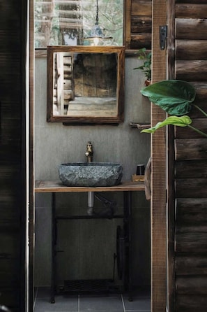 A rustic bathroom with a stone sink, wooden vanity, and a hanging light fixture.
