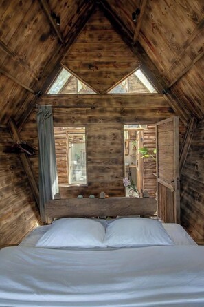 A wooden cabin bedroom with a bed, a window, and a view of the outside.