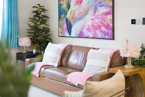 A brown leather sofa with white and pink throw pillows, a pink blanket, and a decorative pink flamingo on a wooden side table. - 3bd golf cart, pool, close to beach (Indian Rocks Beach)