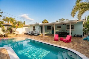 Ein Swimmingpool mit Liegestühlen, eine Terrassenfläche und ein Gebäude mit einer überdachten Außenbereich-Sitzgelegenheit.