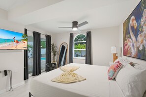 Ein Hotelzimmer mit Bett, Deckenventilator, Fernseher, Fenster mit Vorhängen und einem Gemälde.