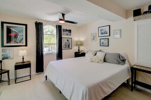 A bedroom with a bed, a ceiling fan, a window with curtains, and wall-mounted artwork.