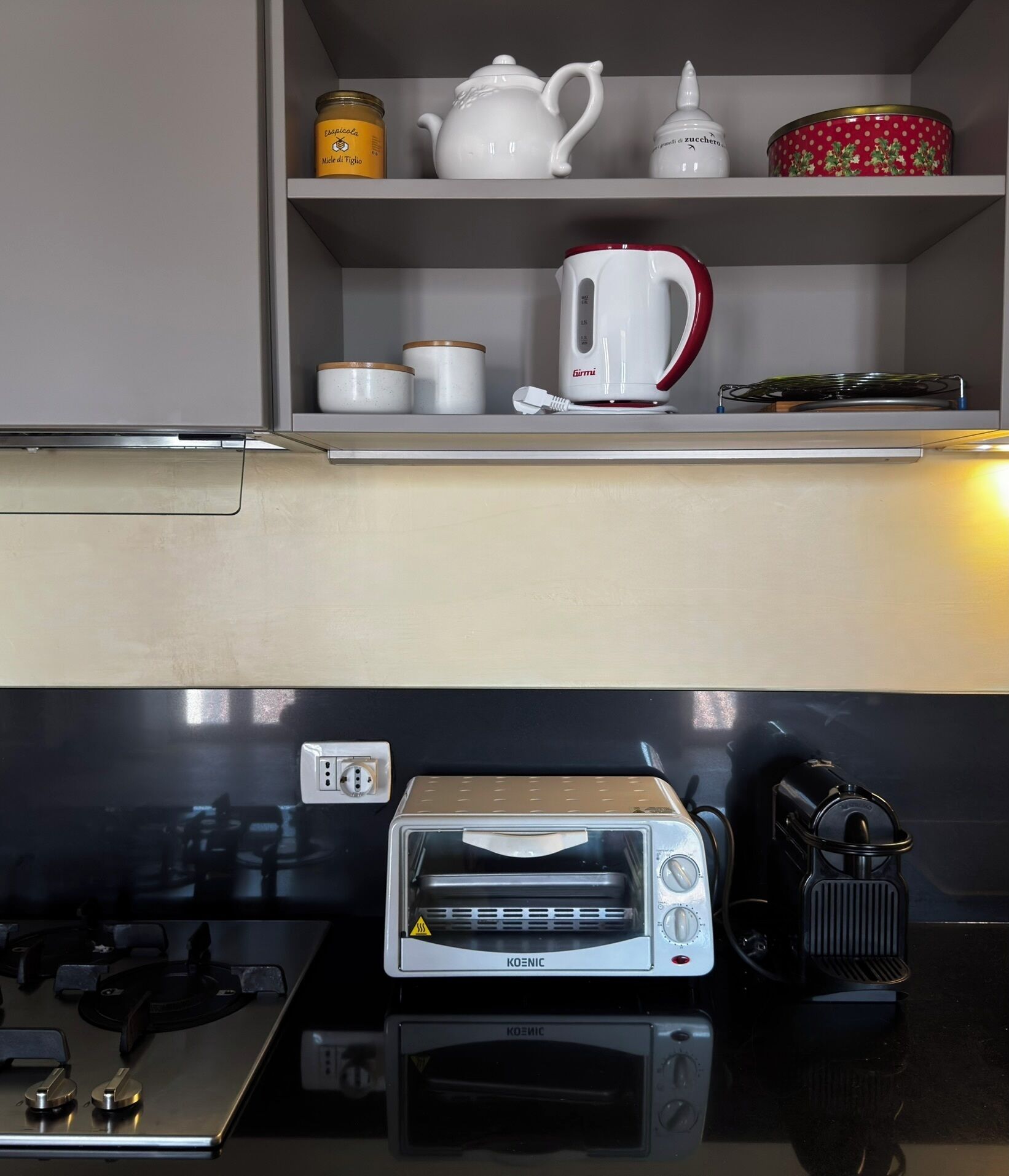 Eine Küche mit weißer Arbeitsplatte, einem roten und weißen Wasserkocher, einem Toaster und einer kleinen Ablage mit Gläsern und einem Teekessel.