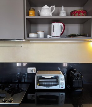 A kitchen with a white countertop, a red and white electric kettle, a toaster, and a small shelf with jars and a teapot. - The House of Mina is in the heart of the small village of Carbognano in Tuscia (Carbognano)