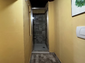 A narrow hallway with a glass door leading to a shower area with a tiled floor.