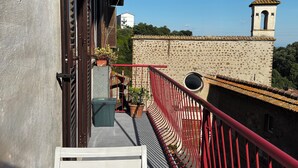A balcony with a red railing, a table with cups, and a view of a building with a bell tower. - The House of Mina is in the heart of the small village of Carbognano in Tuscia (Carbognano)