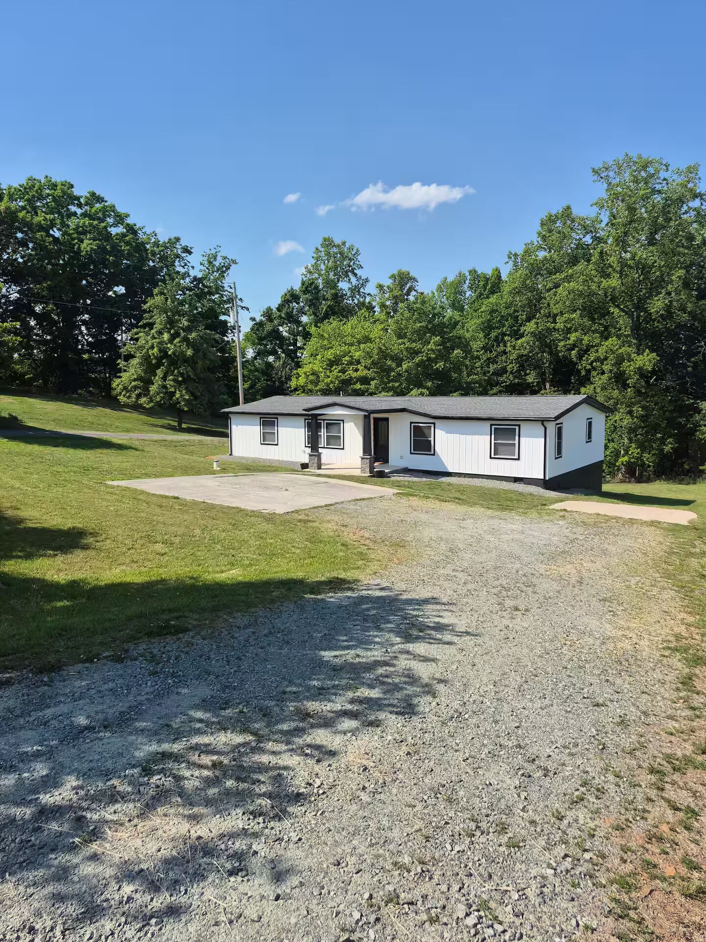 A single-story mobile home with a front porch, a gravel driveway, and a grassy yard.