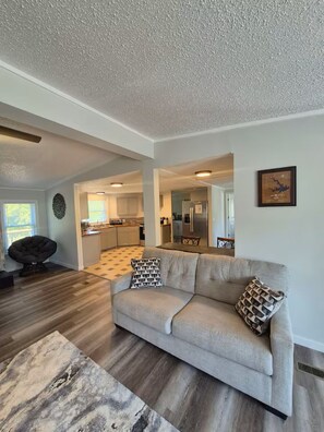 A living room with a sofa, patterned cushions, a rug, and a dining area with a table and chairs. - Lake Life Lodge At Smith Mountain Lake (Moneta)