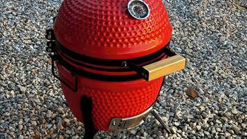 A red barbecue grill with a thermometer and a handle, placed on a gravel surface.