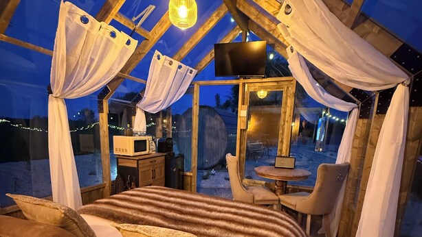 Ein gemütliches, gut beleuchtetes Zelt mit einem Bett, einem Tisch und Stühlen sowie einem an der Wand montierten Fernseher.